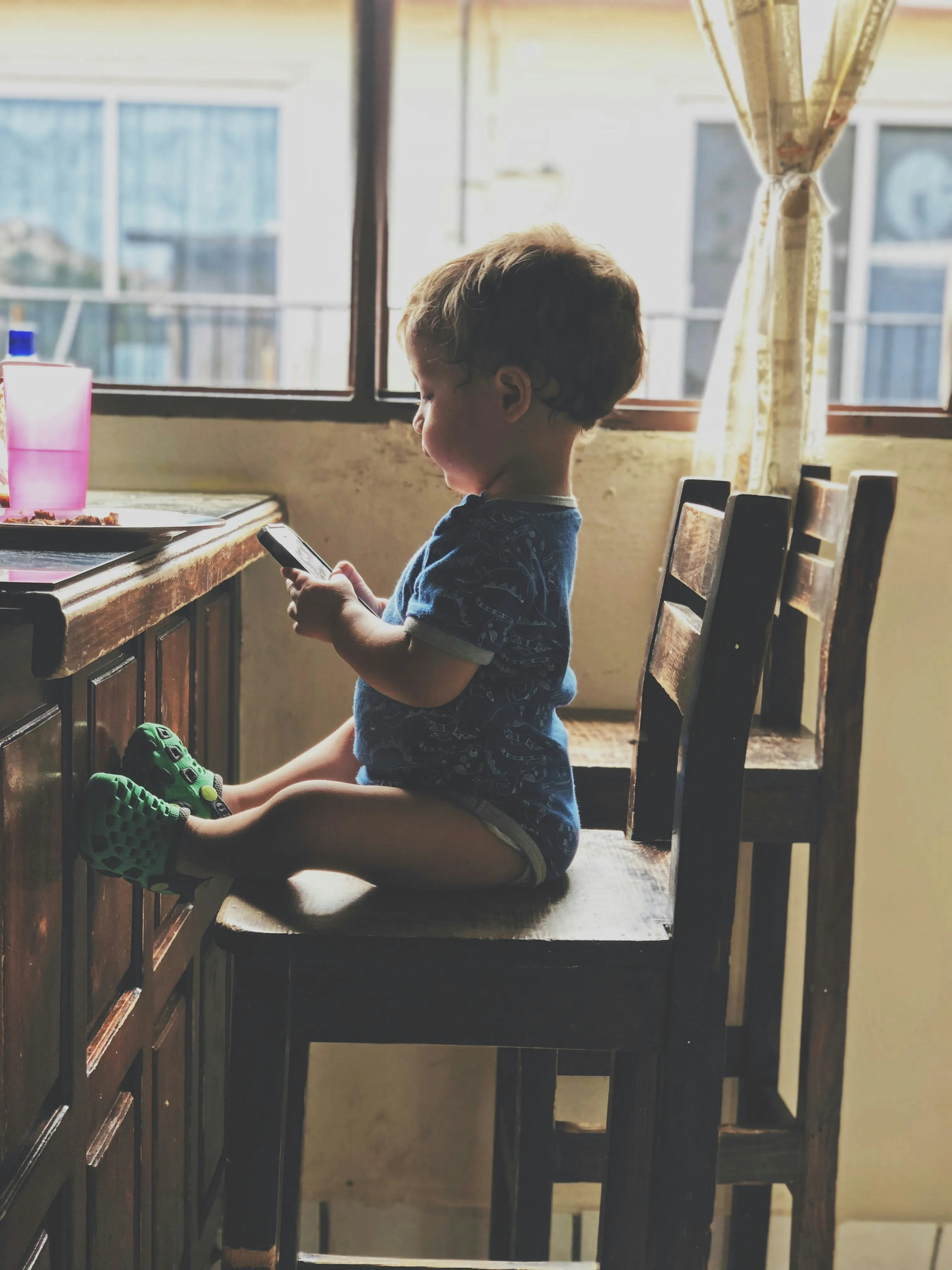 Foto de um bebê sentado mexendo no celular smartphone com filtro vintage.