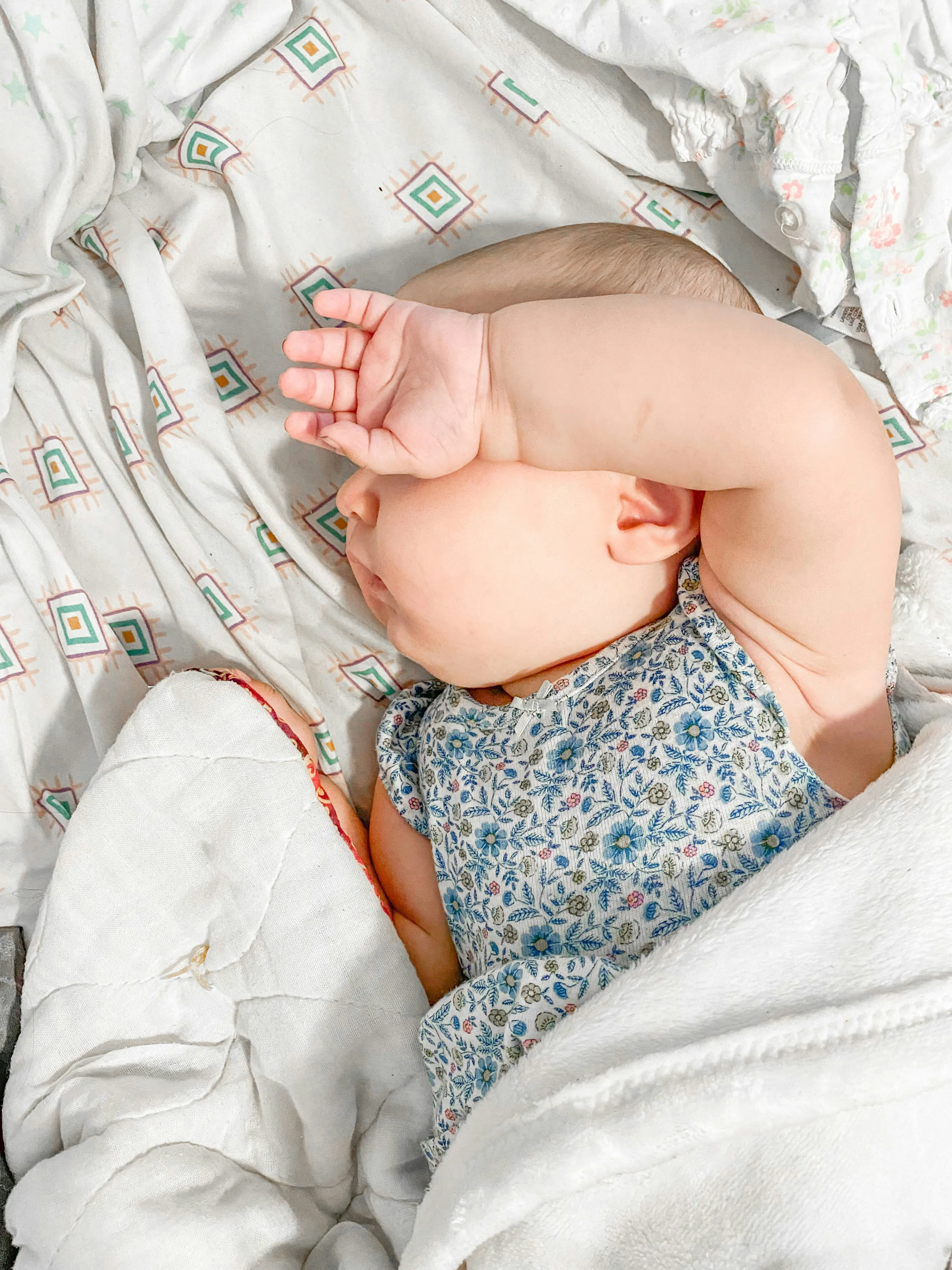 Foto de um bebê fofo dormindo, com a mão tampando o rosto e o produto (caixa de som de ruído branco e sons suaves) posicionado por cima, em alta resolução.